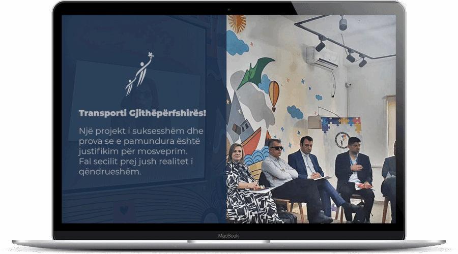 Image showing: Një ekran laptopi shfaq një diapozitiv prezantimi me tekst në shqip dhe një ilustrim në të majtë, ndërsa në të djathtë, disa njerëz ulen në një gjysmërreth në një dhomë të dekoruar me shkëlqim dhe me art mural shumëngjyrësh.